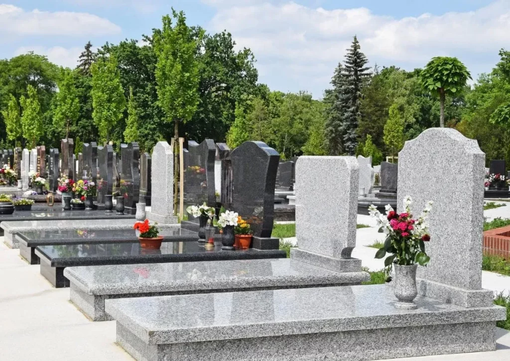 Rangées de monuments funéraires en granit gris dans un cimetière paysager.